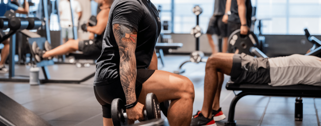 a tattooed man is holding dumbbells in his knee while others are working out