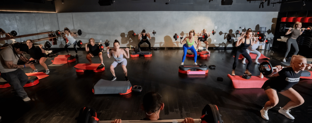 a group of people are following the trainer with a barbell behind their neck in a strength program