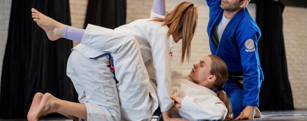 two adult woman are performing martial arts while the trainer seem to teach them how it should be done